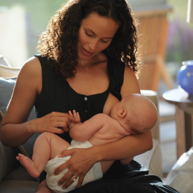 A woman breastfeeding a baby in a nappy, she is wearing a black loose vest top that opens at the side for breast access